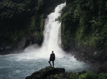 back shot of a man standing in front of a small fall